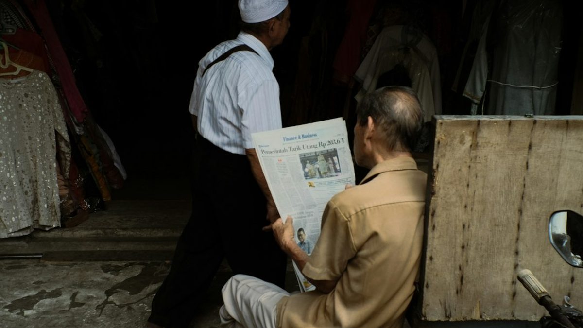 a man sitting on the ground reading a newspaper